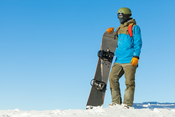 Young snowboarder standing next to snowboard thrusted into snow with clear blue sky behind him