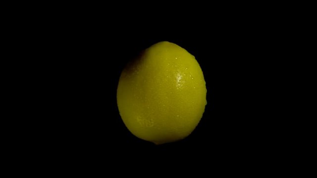 Close-up rotation yellow lemon covered by drops of water. Fresh juicy fruit isolated on black background.
