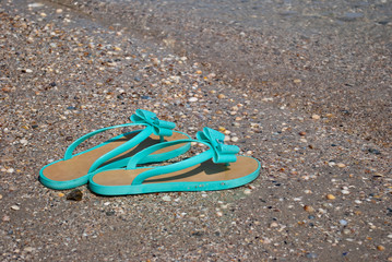 green sea wave mint sneakers of rubber with bows and rhinestones beach slippers on the shore of the blue sea clear water seashells sand blue sky sea wave gale summer vacation weekend
