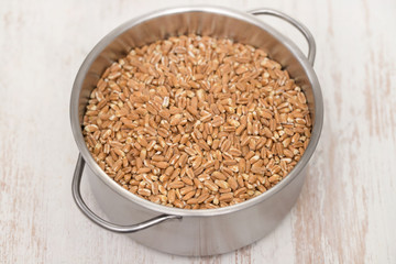 uncooked spelt in pot on wooden background