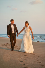 Happy groom and bride walk on beach