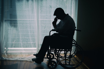 Silhouette of handicapped Man sitting on wheelchair in front of a large panoramic window in hospital,He is sad and lonely. - Powered by Adobe