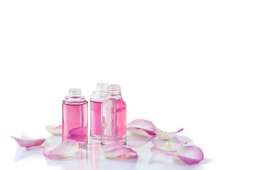 A bottle of rose essential oil with rose petals on white background