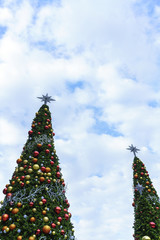 Christmas concept : Decorated artificial Christmas trees with shiny golden , orange and red Christmas balls with white clouds and blue sky background