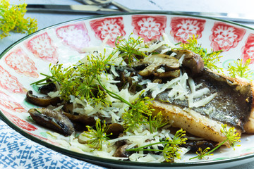 Gebratener Petersfisch mit Dillkraut und Pilzen auf einem Teller mit Besteck im Hintergrund