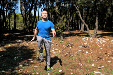 Muscled man doing workout run in place exercise in forest. Handsome sportsman wearing sportswear is running in place exercise in beautiful landscape nature outdoors. Cross fit guy, healthy lifestyle.