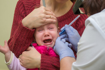Adorable little girl crying very loudly because of having an ear piercing process with special...