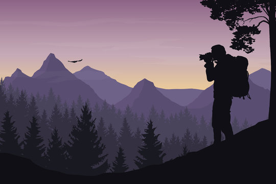 A tourist photographing a flying bird in a mountain landscape with forest under a morning sky with dawn and clouds