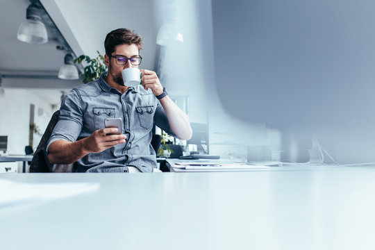 Male designer with mobile phone drinking coffee