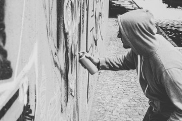 Street graffiti artist painting with a color spray can a graffiti mural on the wall - Urban, lifestyle, street art concept - Black and white edit