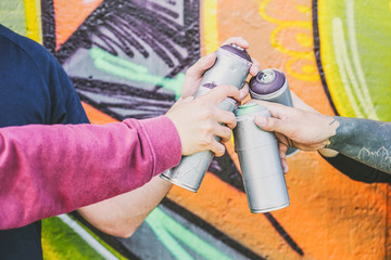 Close up hands of people holding color spray cans against the graffiti wall - Graffiti artists at...