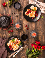 Valentine's day flat lay with delicious pancakes in form of heart, green tea, black teapot, candles and roses. Valentines day concept greeting card. Top view.