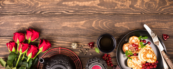 Valentine's day background with delicious pancakes in form of heart, green tea, black teapot, candles and roses. Valentines day concept greeting card. Top view. Copy space. Banner.