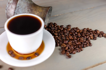 A White Cup of Hot Coffee in a Scattering of Coffee Beans on a Wooden Background