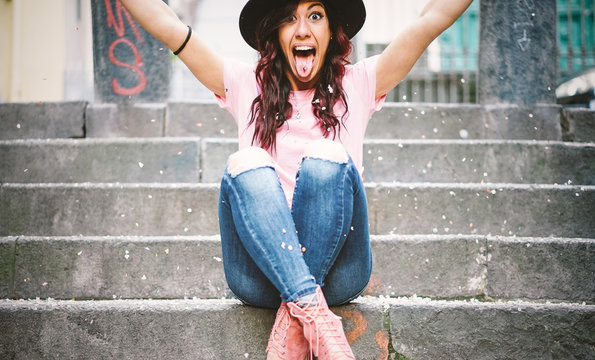 Young hipster woman having fun throwing confetti with her hands - Happy pretty girl celebrating her gratuation sitting on stairs of collage - Vignette edit