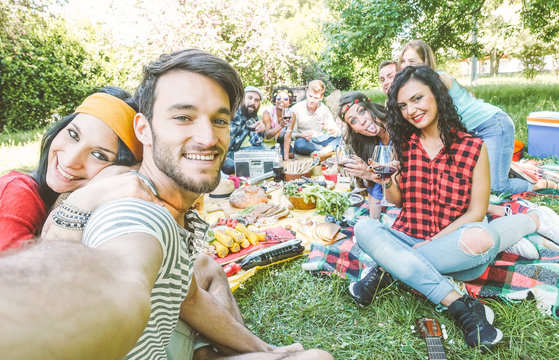 Group of  friends taking a selfie in the park  on a sunny day - Happy people having a picnic eating and drinking wine while taking photo with a mobile phone - Friendship, lifestyle, recreation concept