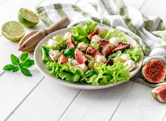 Salad with figs, mozzarella and grapes on a white wooden background.
