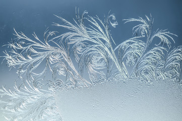 Fototapeta na wymiar Hoarfrost on glass. Winter snowflake pattern on the glass. Frosty pattern on a background of blue sky.