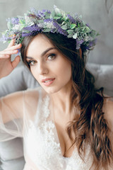 A girl in a beige peignoir, with a wreath of flowers on her head, poses in the studio loft, fine...