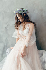 A girl in a beige peignoir, with a wreath of flowers on her head, poses in the studio loft, fine...