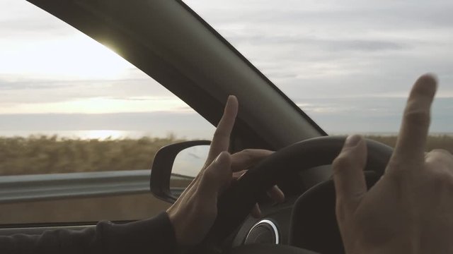 The driver knocks his fingers on the steering wheel in time with the music