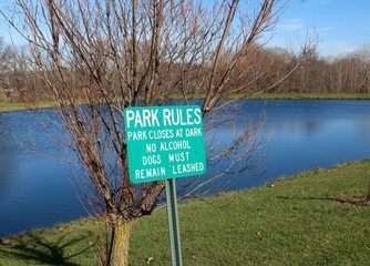 Fototapeta premium The green park rules sign with the lake in the background.