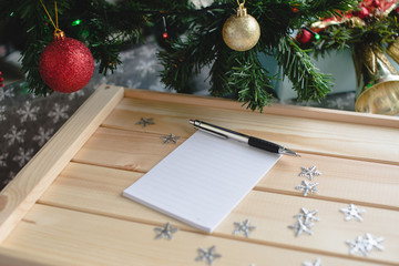 Fototapeta premium Wish list with a pen on the wooden box next to xmas tree. Christmas
