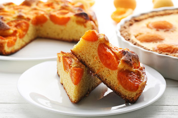 Slices of apricot pie with fruits on white wooden table