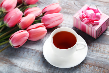 Fototapeta na wymiar Pink tulips with gift box and cup of tea on wooden table