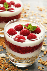 Dessert with raspberries and granola in glasses on grey wooden table