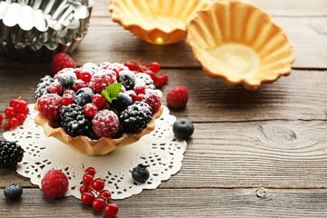 Tasty tartlet with berries and powdered sugar on grey wooden table