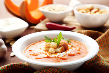 Pumpkin soup with sour cream, rusks and parsley in plate on wooden table