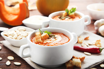 Pumpkin soup with rusks, seeds and parsley in plate on wooden table