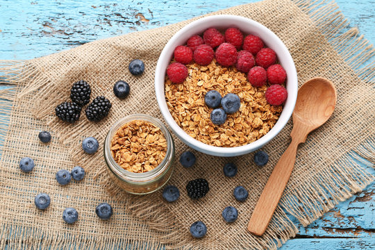 Tasty granola and berries in bowl on blue wooden table