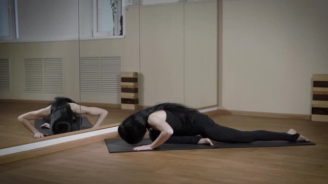 Brunette woman is stretching in yoga class sitting on the mat in fornt of the mirror.