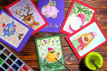 Christmas (New Year) greeting drawn in watercolor handmade postacrads with animals on brown wooden boards. Top view