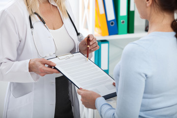 Female doctor holding application form while consulting patient at hospital