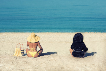 Female in a yellow swimsuit and hat and a girl in a fur coat on the beach. Conceptual picture of winter and summer. Winter is leaving. Summer is leaving. Two seasons winter and summer.