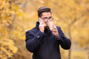 Young handsome man with mobile phone and cup of coffee in park
