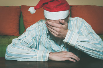 Holiday depression, Young man with Santa Claus hat cover his face with his hands feeling lonely and sad for New Year and Christmas holiday depression concept