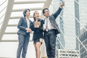 Fototapeta premium young businessmen and two lady in classic suits are holding cups of coffee, talking and smiling, standing outside the office building.