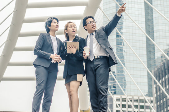 young businessmen and two lady in classic suits are holding cups of coffee, talking and smiling, standing outside the office building.
