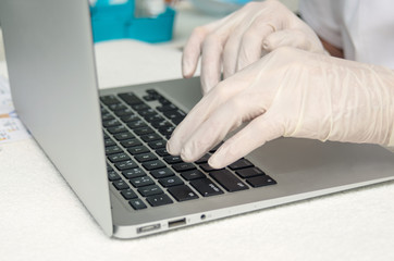 Hands with medical gloves typing on laptop computer.