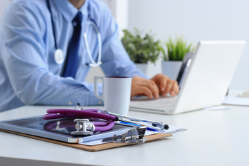 Male doctor using a laptop, sitting at his desk with medical stethoscope