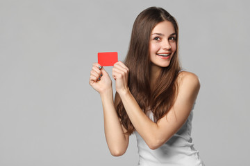 Smiling woman showing blank credit card in white t-shirt, isolated over gray background