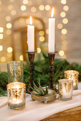 home, cosiness, weekend concept. on the golden shining background there are lots of candles, they have different holders made of glass and black wood and surround small plant with long leaves