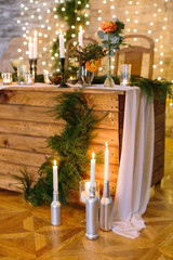 celebrating, birthday, design concept. by the table covered light silk drapping and decorated with flowers, conifers branches, wonderful royal setting there are burning candles on the floorboards