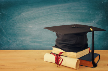 Image of graduation black hat over old books next to graduation on wooden desk. Education and back...