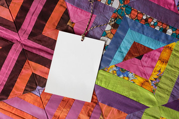 handcraft, creating, gifting concept. there is white clean card for greeting on amazing quilt of marvelous bright colours and with different floral and geometric patterns