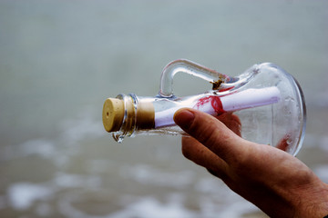 A man's hand with a glass vessel against the sea